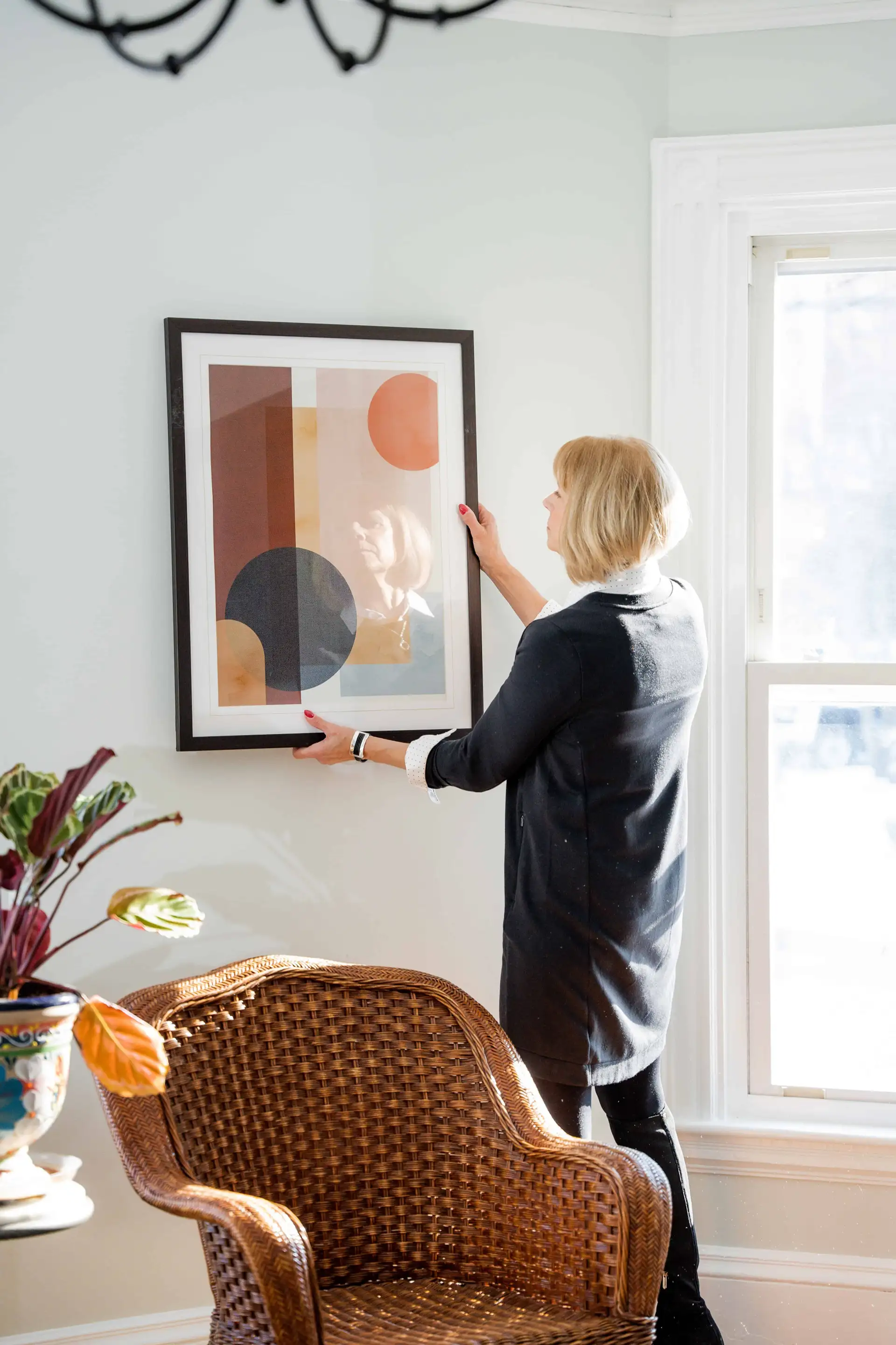 A woman is fixing a picture on the wall.