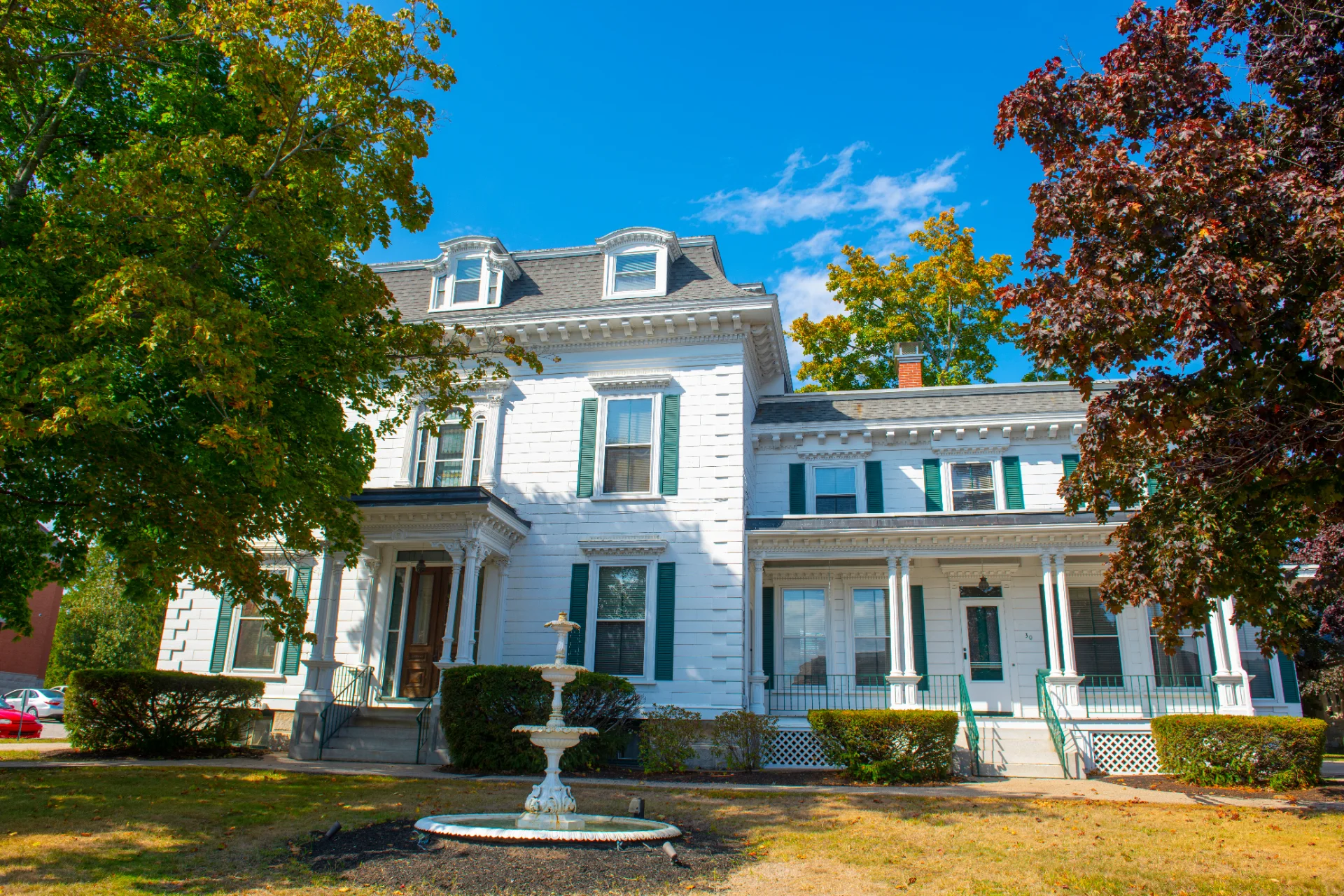 White Second Empire historic home with a mansard roof and a garden fountain