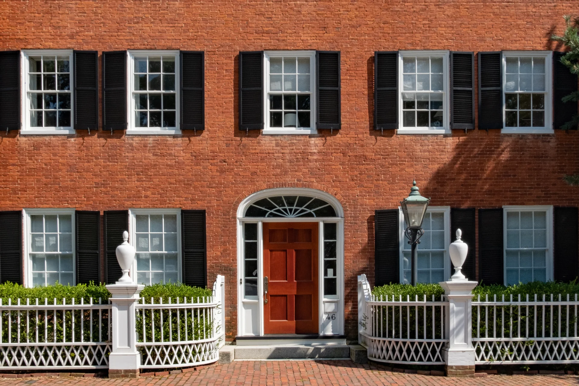Brick Federal home with black shutters, a fanlight doorway and a white picket fence