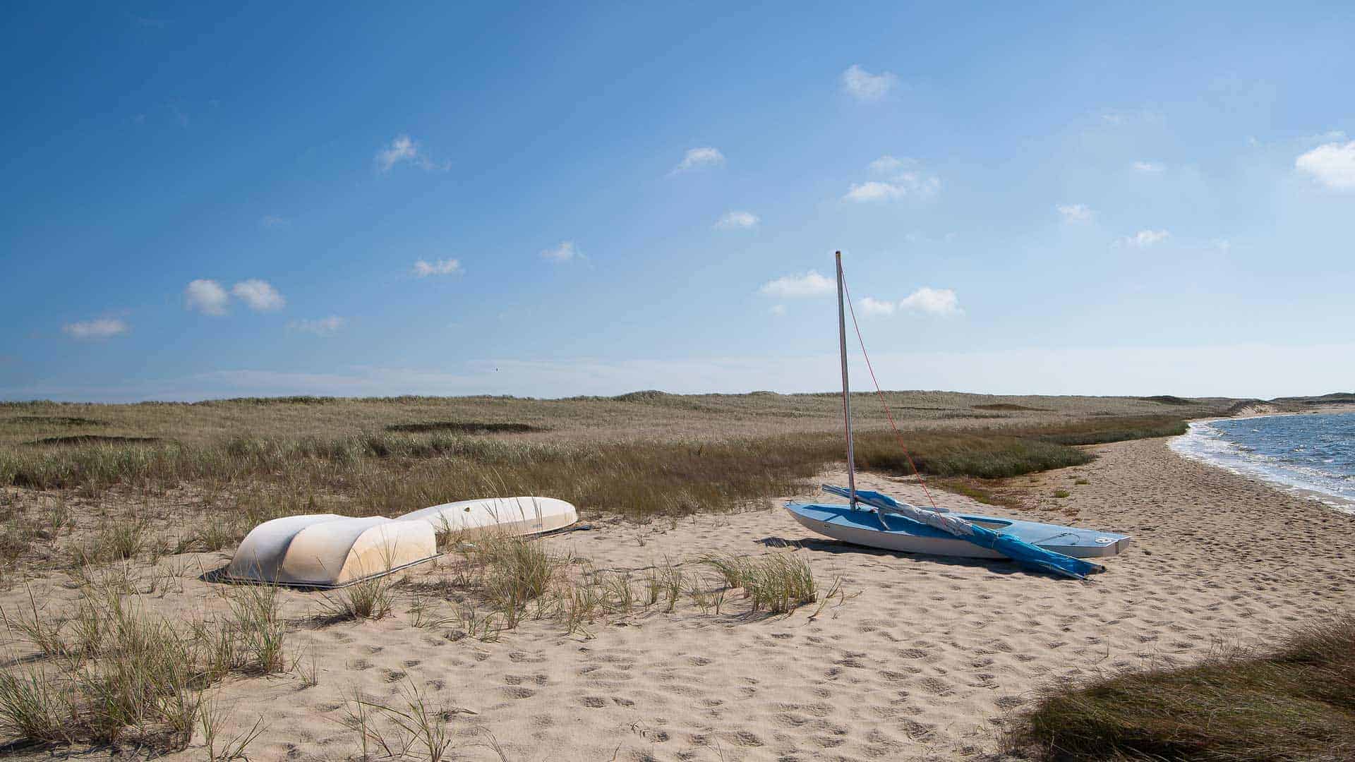 Sandy beach and blue skies with two small old boats on shore.