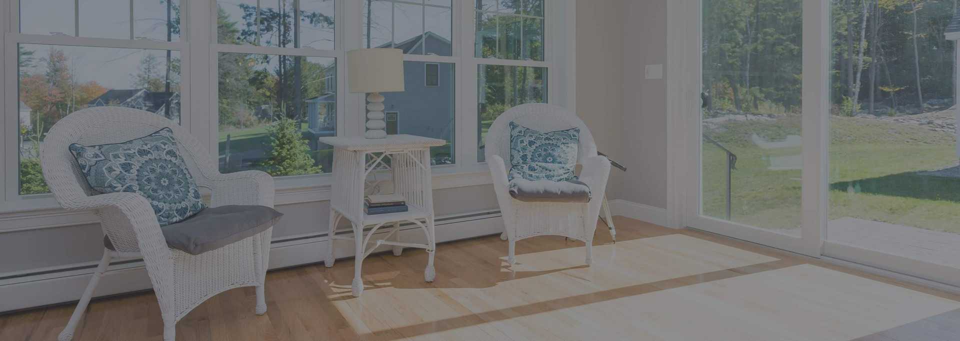 White wicker furniture in sun room with large windows and wood floors.