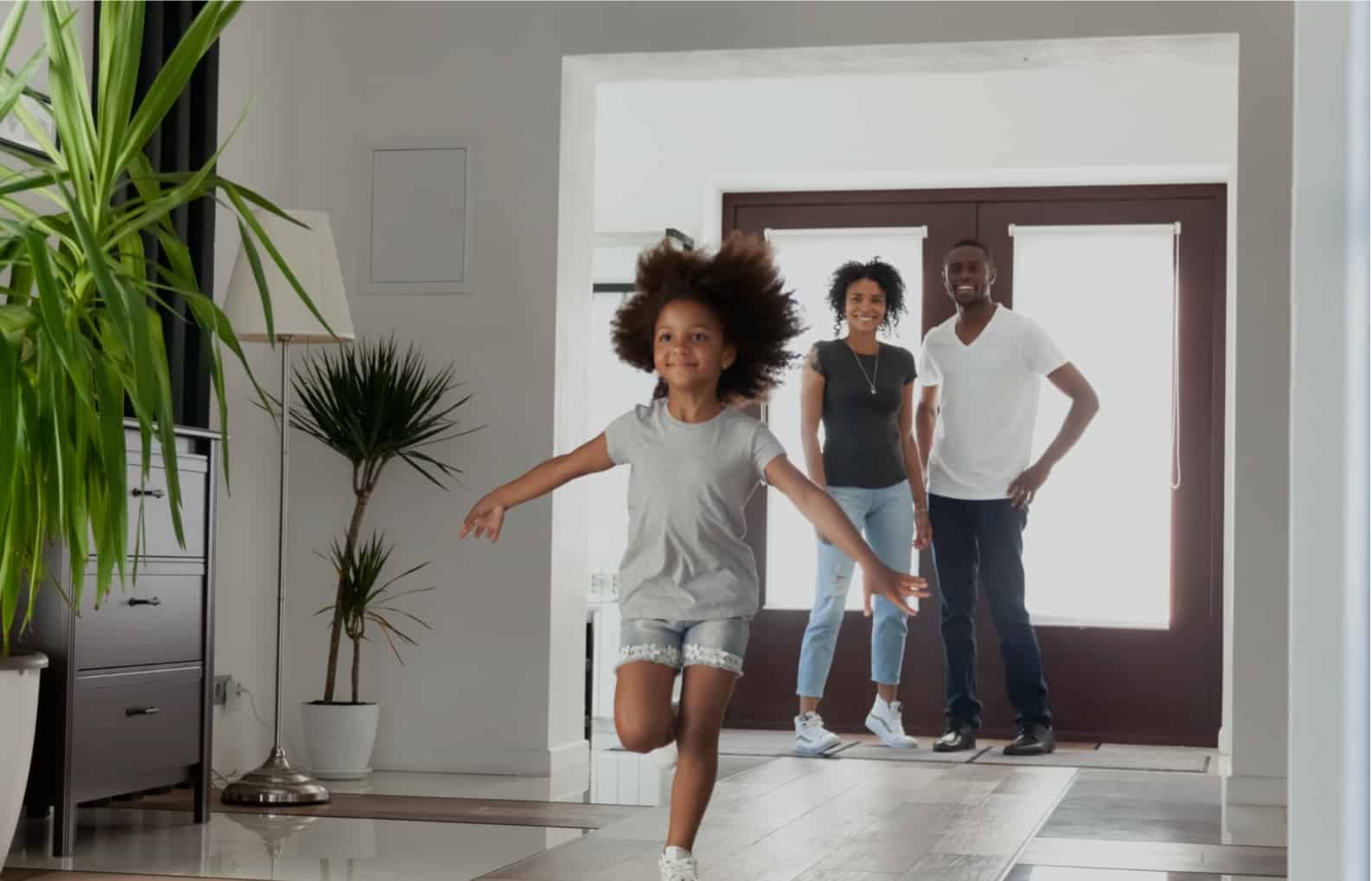 Family of three inside new home with child running down hallway smiling