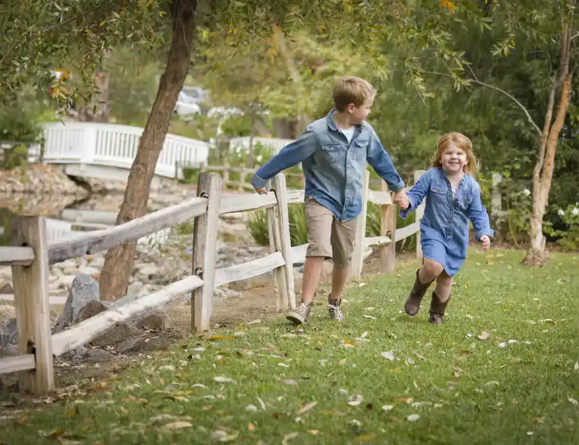 two children holding hands and running next to fence.