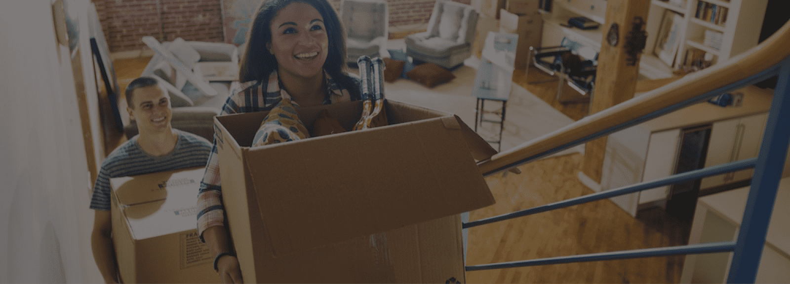 Two people smiling while carrying moving boxes up stairs